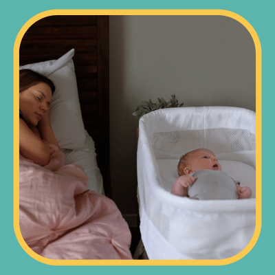 Baby asleep in bassinet next to parent in bed.